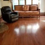 A cozy living space with warm, reddish-brown hardwood floors, a black recliner, and a traditional patterned sofa.