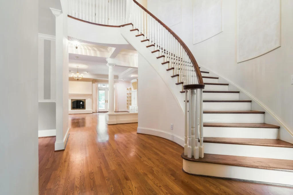 A grand, white curved staircase with dark wood treads leading into a spacious foyer with polished hardwood floors.