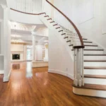 A grand, white curved staircase with dark wood treads leading into a spacious foyer with polished hardwood floors.
