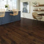 A modern kitchen and dining area featuring deep brown hardwood floors, blue cabinetry, and wicker barstools.